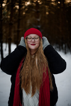 Smiling young woman in winter outfit holding pine branches outdoors in snowy forest. Concept of Christmas holidays, winter lifestyle, happiness, seasonal nature and festive mood.