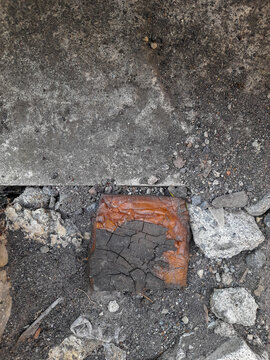 Top view of a square piece of rubberwood cracked and partially charred resting on a rough concrete surface