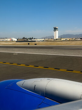 BURBANK, CA, APR 28, 2026: Airplane wing and engine cowling on the tarmac, with a control tower and taxiway in the background under clear sky