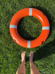 Lifebuoy on grass with bare feet visible, summer safety equipment © Лена Шевчук