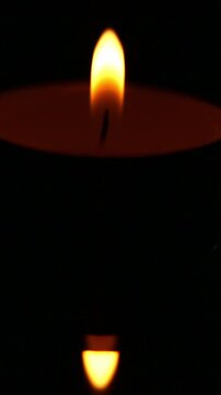 Lighting a candle. The candle flame wavers and flickers briefly with rising smoke before turning into a calm, luminous fire burning steadily above a small tea light in the darkness.