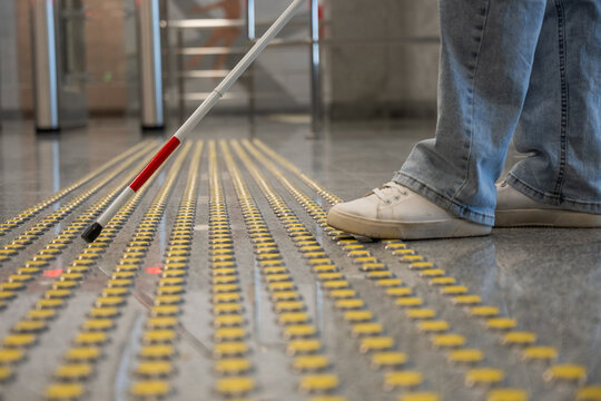 A blind woman walks on tactile paving. Close-up of her feet and a walking stick.