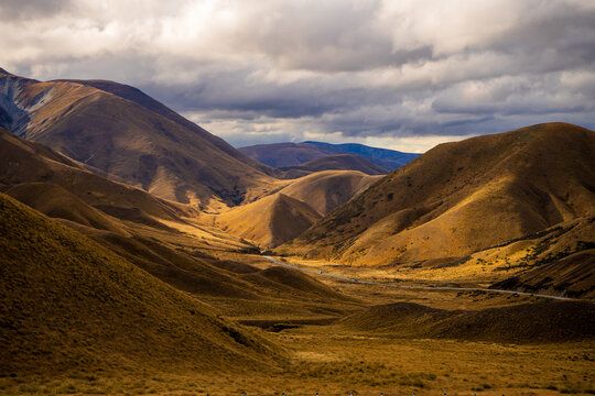 Golden tussock hills and a winding highway through a high mountain pass, New Zealand
