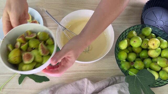 Hands work at a light wood table surface preparing food items, small green pieces are arranged on white plates and in bowls alongside yellow liquid mixtures