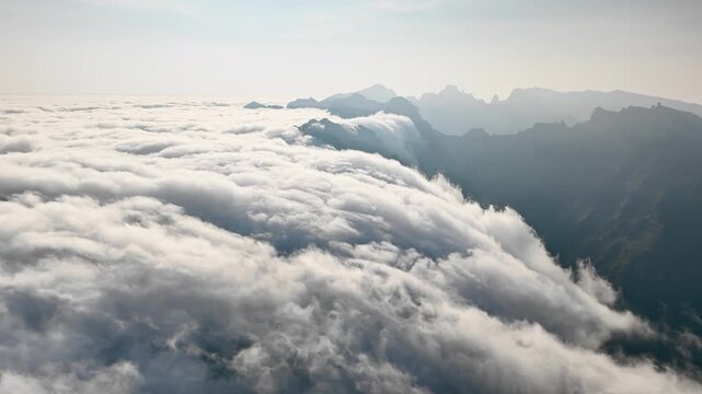 Dense moving clouds over mountain valleys, aerial view. Mountain summits remain above cloud layer