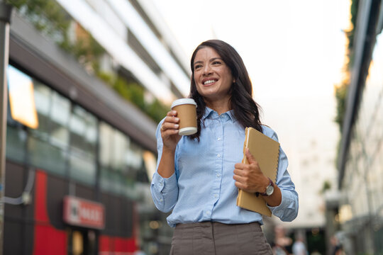 Professional businesswoman smiling walking with coffee and notebook
