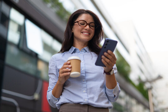 Businesswoman checking smartphone and drinking coffee outdoors