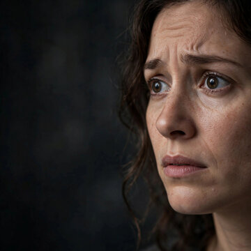 Close up of worried woman with wide anxious eyes and dark copy space background fear emotion