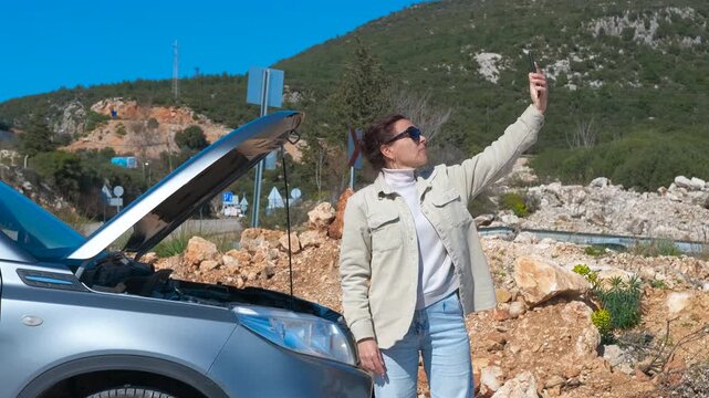 Woman searching for cell signal with broken car. Stressed woman with a broken car searching for a cell phone signal on a mountain road, trying to make an emergency call for roadside assistance