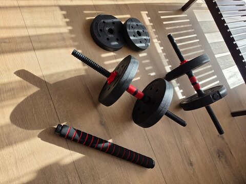 ​Adjustable dumbbells, extra weight plates, and fitness accessory on a wooden floor in a sunny room for home training