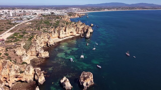 Boats anchored near Ponta da Piedade cliffs and turquoise coves on the Algarve coast, aerial drone view, Lagos, Portugal
