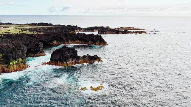 Jagged lava rocks line Atlantic shore of Sao Miguel, Azores, Portugal. Close aerial footage of solidified lava formations along rugged volcanic coastline beside open ocean