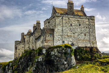 Historic stone fortress perched on rugged volcanic rock promontory, traditional lime mortar masonry and turrets overlooking grassy slopes © whitcomberd