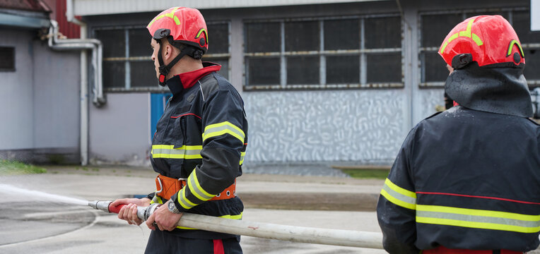 Firefighters Working Together With Hose During Outdoor Training Drill At Industrial Fire Station