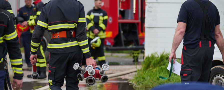 Firefighters Carrying Hydrant Manifold During Emergency Response Drill With Fire Engine And Crew Teamwork