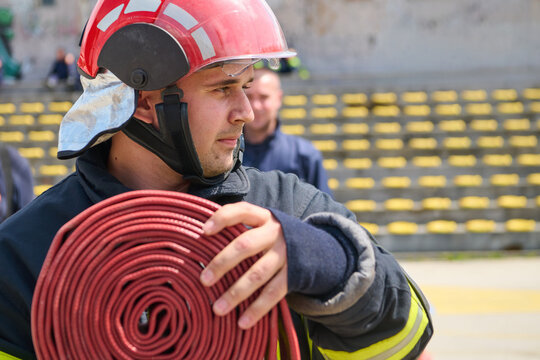Firefighter Carrying Coiled Fire Hose Wearing Red Helmet And Protective Turnout Gear During Drill