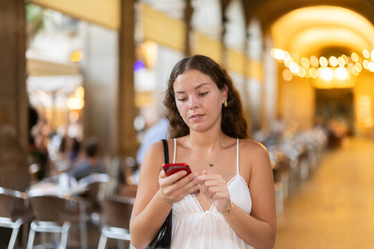 Young woman in summer clothes and with a phone in hands walks through the streets of Barcelona, she wants to meet friends and go to a restaurant in the evening