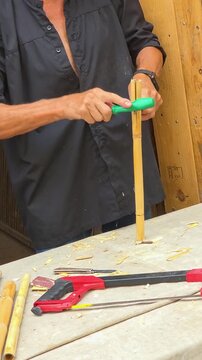 Close up shot of artisan handcrafting a traditional reed musical instrument dolcaina or xirimita from giant reed stalk at a Spanish cultural festival.