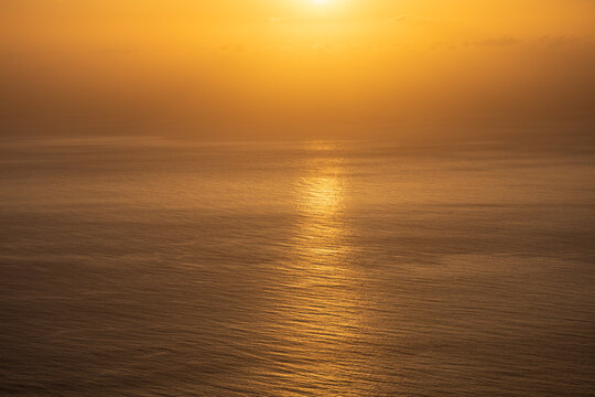 Golden sunset over calm ocean water with bright sun reflection and haze background