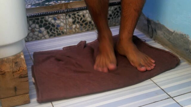 a person's feet standing on a brown towel on a tiled bathroom floor