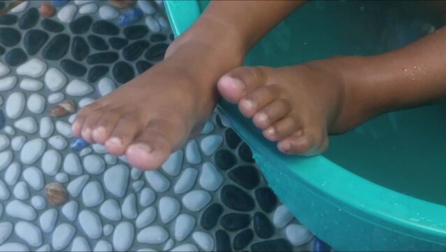 A small child's feet are soaking in a green plastic tub filled with water.
