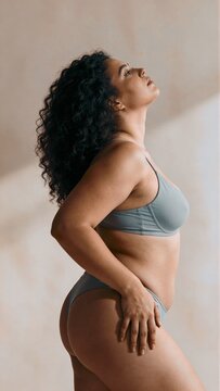 Confident woman with curly hair in grey bodysuit posing in side view