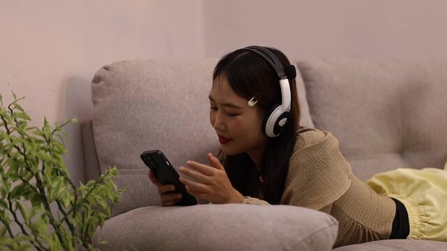 Asian Woman Relaxing at Home Using Smartphone While Listening to Music