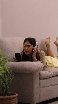 Asian Woman Relaxing at Home Using Smartphone While Listening to Music