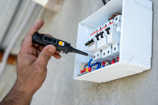The hand of an electrician using a multimeter to check electrical connections in a junction box.