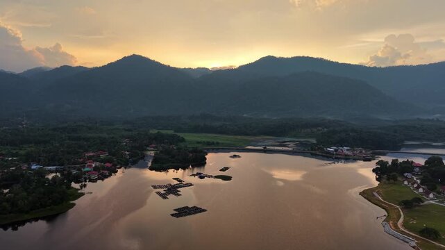 Aerial drone shot captures golden hour over calm lake. Reflections mirror distant mountains and sky at Tasik Raban