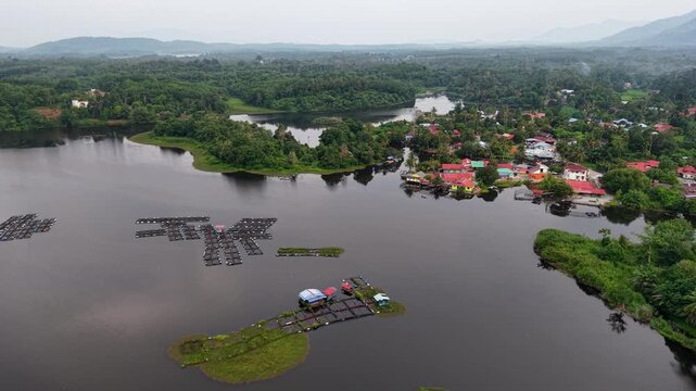Aerial view of tranquil lake surrounded by lush greenery. Floating structures dot calm waters at Tasik Raban