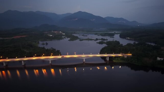 Glowing bridge lights reflect on calm water at dusk at Tasik Raban