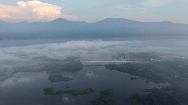 Serene early morning view of a river surrounded by mist, mountains, and a distant bridge at Tasik Raban