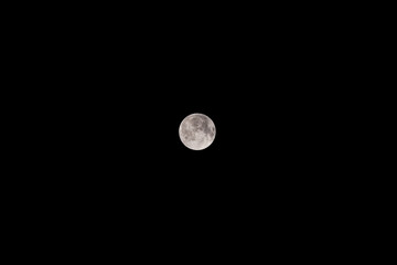 A detailed full moon with visible surface craters, set against a completely dark black night sky. Clear astronomical view of the lunar satellite. © tai