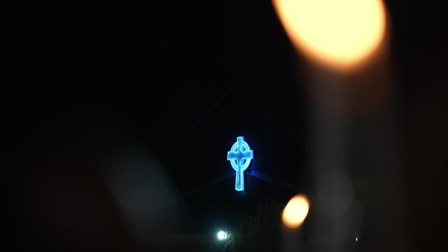 Nighttime slow motion ground view of illuminated blue cross with bokeh lights at Saint Anne festival.