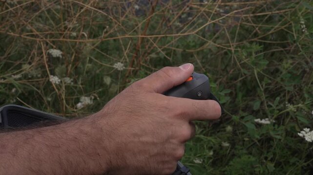 Man controlling a drone outdoors with a handheld joystick controller, focusing on his hands and the remote device. Modern aerial technology and outdoor drone piloting concept