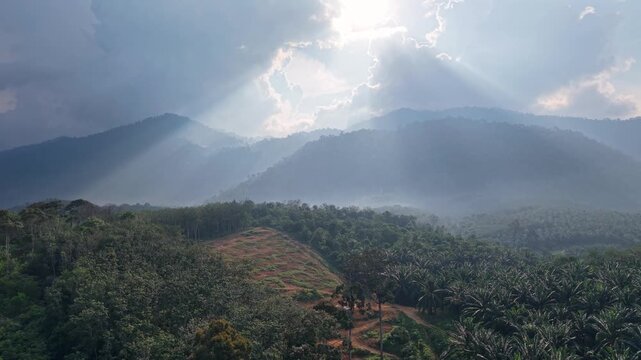 Bright sunlight breaks through a cloudy sky illuminating a lush green mountain forest with mist and atmospheric layers in this tranquil natural landscape at Tasik Raban