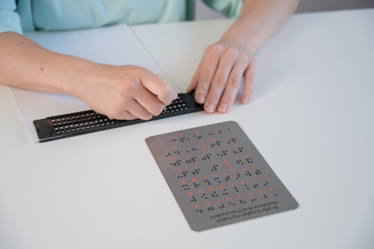 A blind woman writes in Braille using a stencil on a piece of paper. 