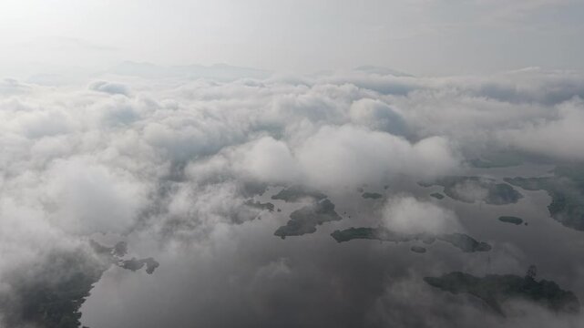 High altitude view shows clouds as a sea above islands. Sunlight pierces cloud cover at Tasik Raban