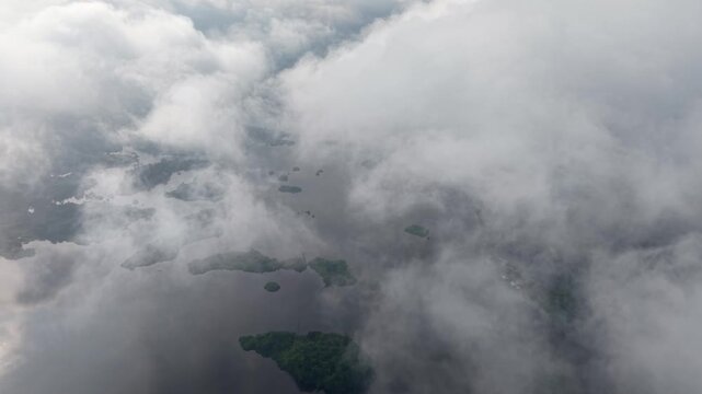 Aerial view of a foggy landscape featuring calm river water and a green forest island partially hidden by mist at Tasik Raban