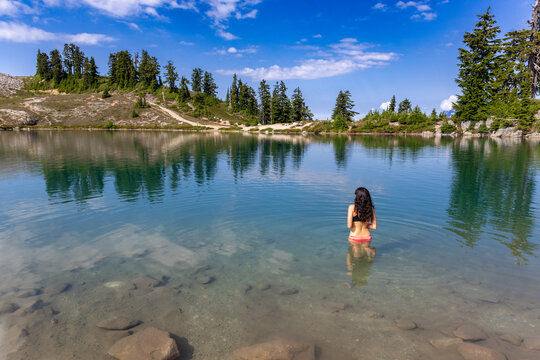 Woman wading in a clear alpine lake beneath a blue sky