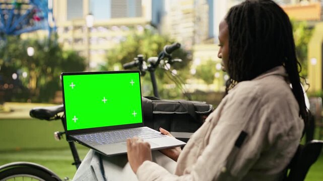 Smartphone with an isolated green screen mockup is held by a woman in an urban park, providing a replaceable widescreen display for website and advertising content with screen replacement.