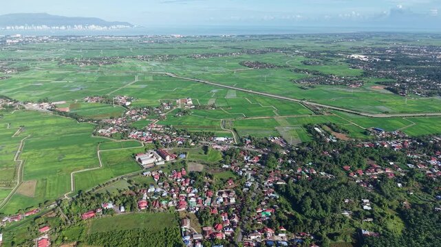 An aerial perspective showcases expansive green fields, a small village, and surrounding forests at Kubang Semang