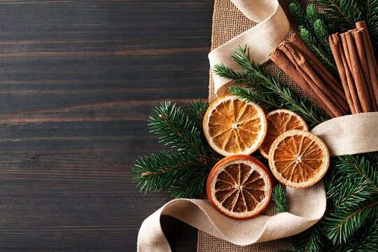 Warm brown wooden tabletop decorated with dried oranges, cinnamon sticks, fir branches, and beige ribbon