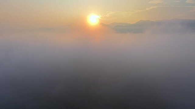 Golden sun rises above clouds. Thick fog blankets distant hills