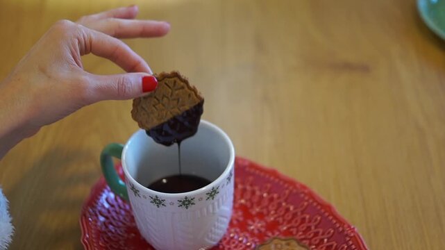 Close-up of female hands carefully placing a freshly chocolate-coated gingerbread cookie onto a baking sheet decorated with holiday elements.
