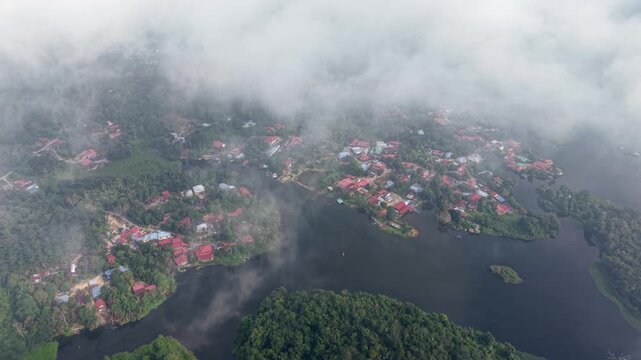 Aerial shot reveals foggy clouds above a lakeside village at Tasik Raban