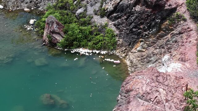 Top down drone shot of rocky reservoir shoreline littered with plastic and foam debris