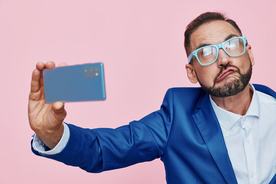 A confident business professional takes a selfie against a solid pink background, isolated color field, projecting focus, charm, and a hint of curiosity.