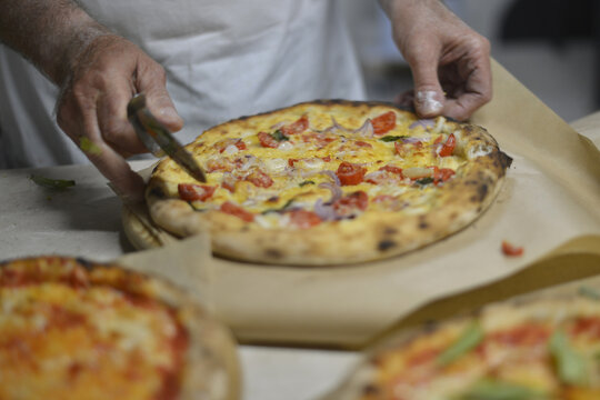pizzaiolo taglia la pizza prima di servirla al cliente della pizzeria